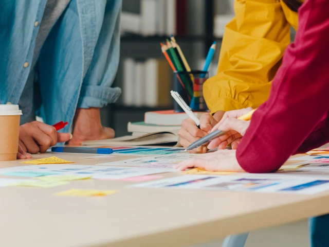 People around a table point at design thinking materials like post it notes.